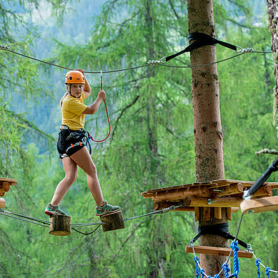 Mädchen klettert im Hochseilgarten in Tirol.